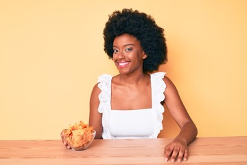 Young african american woman holding nachos potato chips looking positive and happy standing and smiling with a confident smile showing teeth