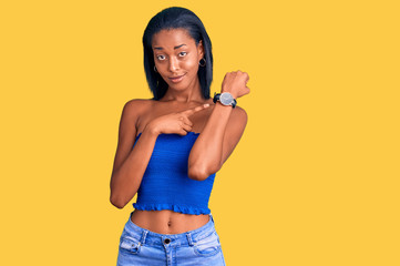Young african american woman wearing casual summer clothes in hurry pointing to watch time,...
