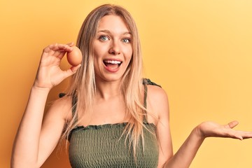 Young blonde woman holding egg celebrating achievement with happy smile and winner expression with raised hand