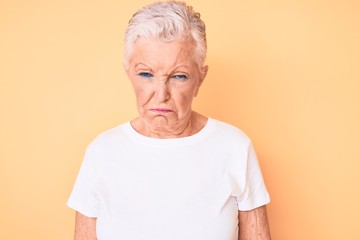 Senior beautiful woman with blue eyes and grey hair wearing classic white tshirt over yellow background depressed and worry for distress, crying angry and afraid. sad expression.