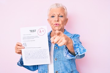 Senior beautiful woman with blue eyes and grey hair showing a passed exam pointing with finger to the camera and to you, confident gesture looking serious