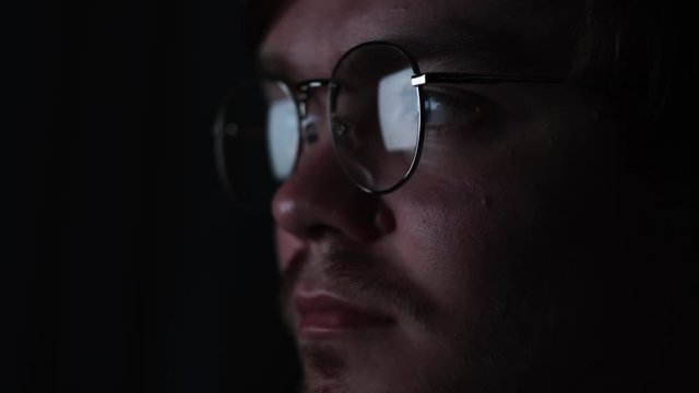 Business man, coder or programmer working late at night with laptop. Concept. Thoughtful focused guy in the dark with the computer screen reflected in his glasses.