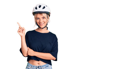 Young beautiful blonde woman wearing bike helmet smiling happy pointing with hand and finger to the side