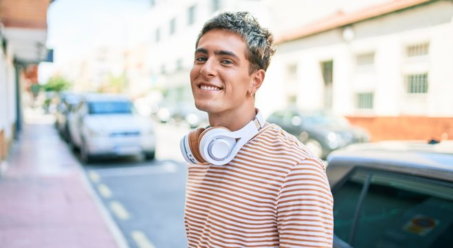 Young handsome caucasian man smiling happy wearing headphones walking at city.