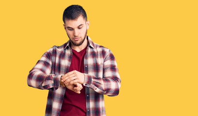 Young handsome man wearing casual shirt checking the time on wrist watch, relaxed and confident