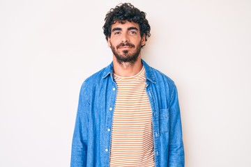 Handsome young man with curly hair and bear wearing casual denim jacket relaxed with serious expression on face. simple and natural looking at the camera.