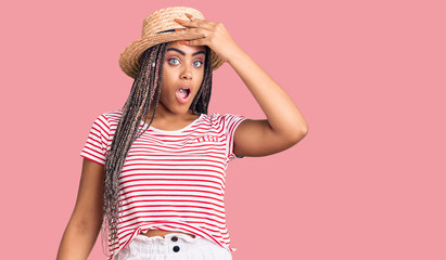 Young african american woman with braids wearing summer hat surprised with hand on head for...