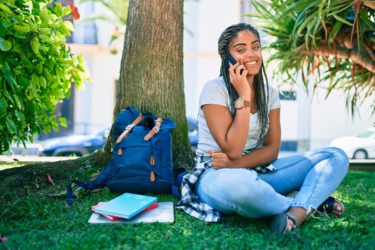 Young african american student woman smiling happy speaking on smartphone sitting on the grass at the university campus