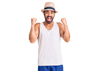 Naklejka premium Young hispanic man wearing casual summer hat celebrating surprised and amazed for success with arms raised and open eyes. winner concept.