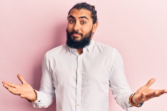 Young arab man wearing casual clothes clueless and confused expression with arms and hands raised. doubt concept.