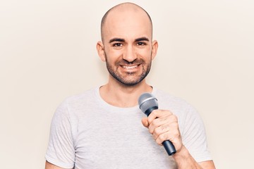 Naklejka premium Young handsome bald man singing song using microphone looking positive and happy standing and smiling with a confident smile showing teeth
