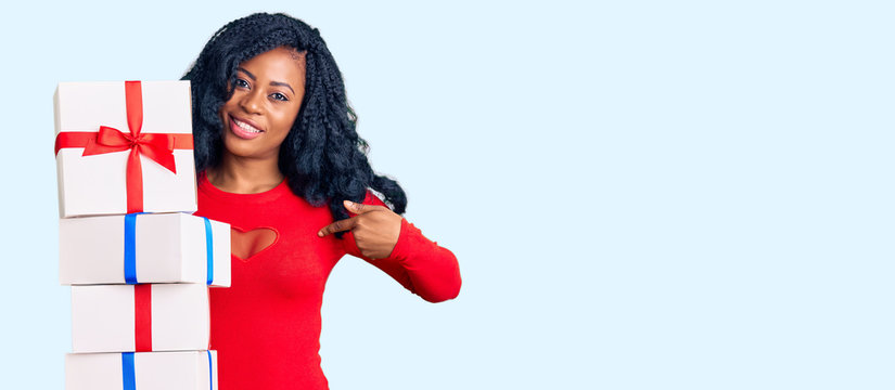 Beautiful african american woman holding presents pointing finger to one self smiling happy and proud