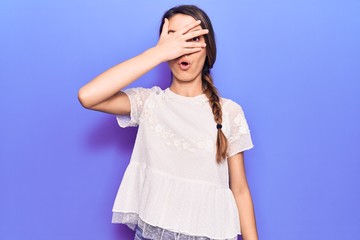 Young beautiful girl wearing casual t-shirt peeking in shock covering face and eyes with hand, looking through fingers afraid