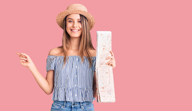 Young beautiful girl wearing hat holding city map smiling happy pointing with hand and finger to the side