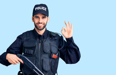 Young handsome man with beard wearing police uniform holding shotgun doing ok sign with fingers, smiling friendly gesturing excellent symbol