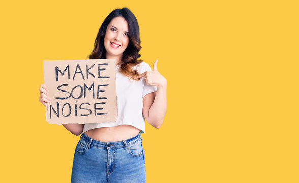 Beautiful young brunette woman holding make some noise banner pointing finger to one self smiling happy and proud
