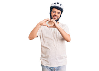 Young hispanic man wearing bike helmet smiling in love showing heart symbol and shape with hands. romantic concept.