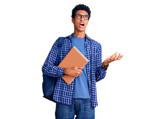 Young african american man wearing student backpack holding book crazy and mad shouting and yelling with aggressive expression and arms raised. frustration concept.