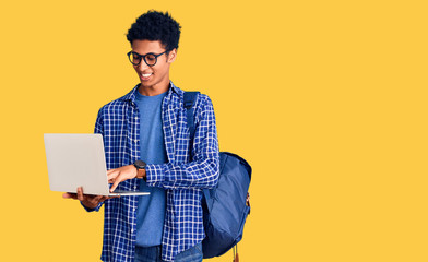 Young african american man holding student backpack using laptop looking positive and happy standing and smiling with a confident smile showing teeth - obrazy, fototapety, plakaty