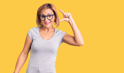 Young blonde woman wearing casual clothes smiling and confident gesturing with hand doing small size sign with fingers looking and the camera. measure concept.