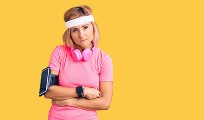 Young blonde woman wearing sportswear and headphones skeptic and nervous, disapproving expression on face with crossed arms. negative person.