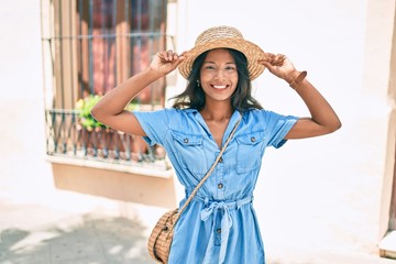 Obraz premium Young beautiful indian woman wearing summer hat smiling happy walking at the city.
