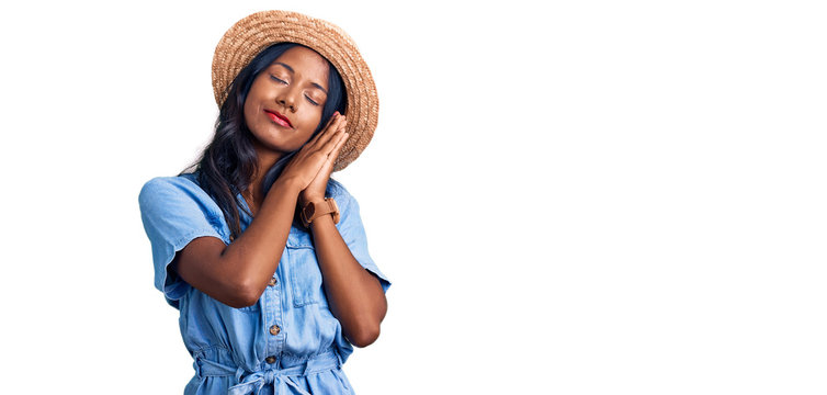 Young indian girl wearing summer hat sleeping tired dreaming and posing with hands together while smiling with closed eyes.