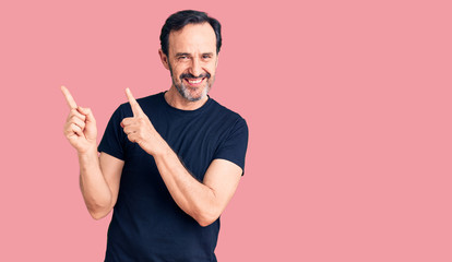 Middle age handsome man wearing casual t-shirt smiling and looking at the camera pointing with two hands and fingers to the side.