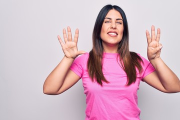 Young beautiful brunette woman wearing casual pink t-shirt standing over white background showing and pointing up with fingers number eight while smiling confident and happy.