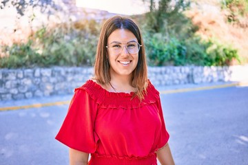 Young beautiful woman wearing casual dress and glasses smiling happy. Standing with smile on face walking at street of city.