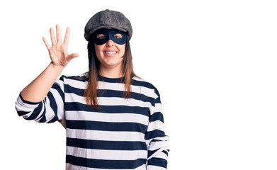 Young beautiful brunette woman wearing burglar mask showing and pointing up with fingers number five while smiling confident and happy.
