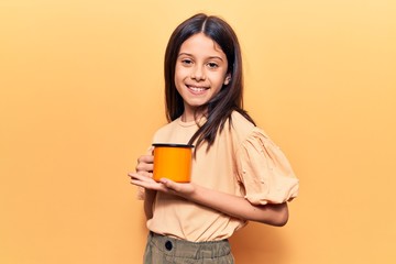 Fototapeta premium Beautiful child girl holding coffee looking positive and happy standing and smiling with a confident smile showing teeth