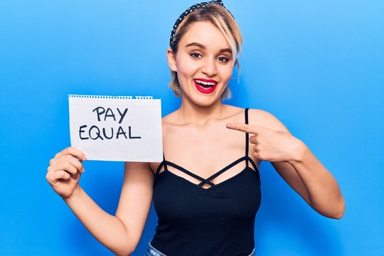 Young beautiful blonde woman holding pay equal paper smiling happy pointing with hand and finger