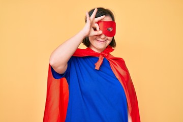 Brunette woman with down syndrome wearing super hero costume smiling happy doing ok sign with hand...