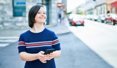 Beautiful brunette woman with down syndrome at the town on a sunny day using smartphone