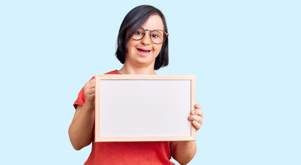 Fototapeta premium Brunette woman with down syndrome holding empty white chalkboard screaming proud, celebrating victory and success very excited with raised arms