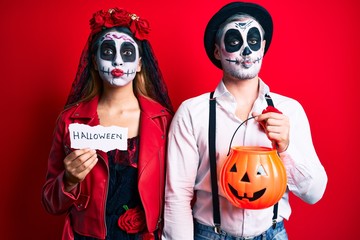 Couple wearing day of the dead costume holding pumpking and halloween paper puffing cheeks with funny face. mouth inflated with air, catching air.