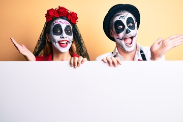 Couple wearing day of the dead costume holding blank empty banner celebrating achievement with happy smile and winner expression with raised hand