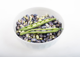 Blue and green peas from inside green string bean pod in a white bowl