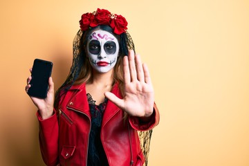 Woman wearing day of the dead costume holding smartphone showing screen with open hand doing stop...