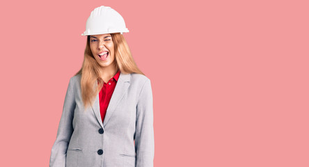 Beautiful young woman wearing architect hardhat winking looking at the camera with sexy expression,...