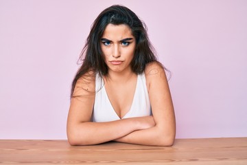 Brunette teenager girl wearing casual clothes sitting on the table skeptic and nervous, disapproving expression on face with crossed arms. negative person.