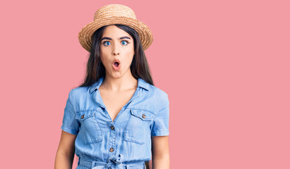 Brunette teenager girl wearing summer hat afraid and shocked with surprise expression, fear and excited face.