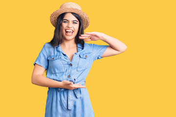 Brunette teenager girl wearing summer hat gesturing with hands showing big and large size sign, measure symbol. smiling looking at the camera. measuring concept.