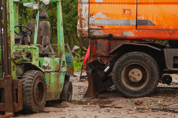 The area of reception of scrap metal, the orange excavator and green truck waiting for work, the concept of garbage.