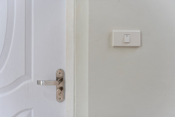 White lighting switches on wall and door handle on wall at home.