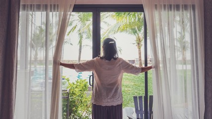 Asian senior women are staying in a hotel room.Open the curtain and  door in the room looking to outside view.Travel in holidays weekend concept.Vintage tone.