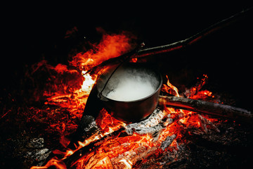 The hot tea pot is heated at the campfire.