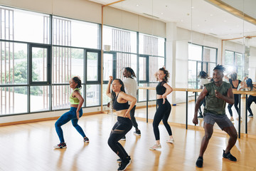 Group of joyful dancers practicing new movement when rehearsing in studio