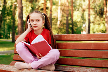 Little Girl Rest On Park Bench And Talk By Phone. Concept Of Speaking By Modern Gadgets And Fast Internet In Park.